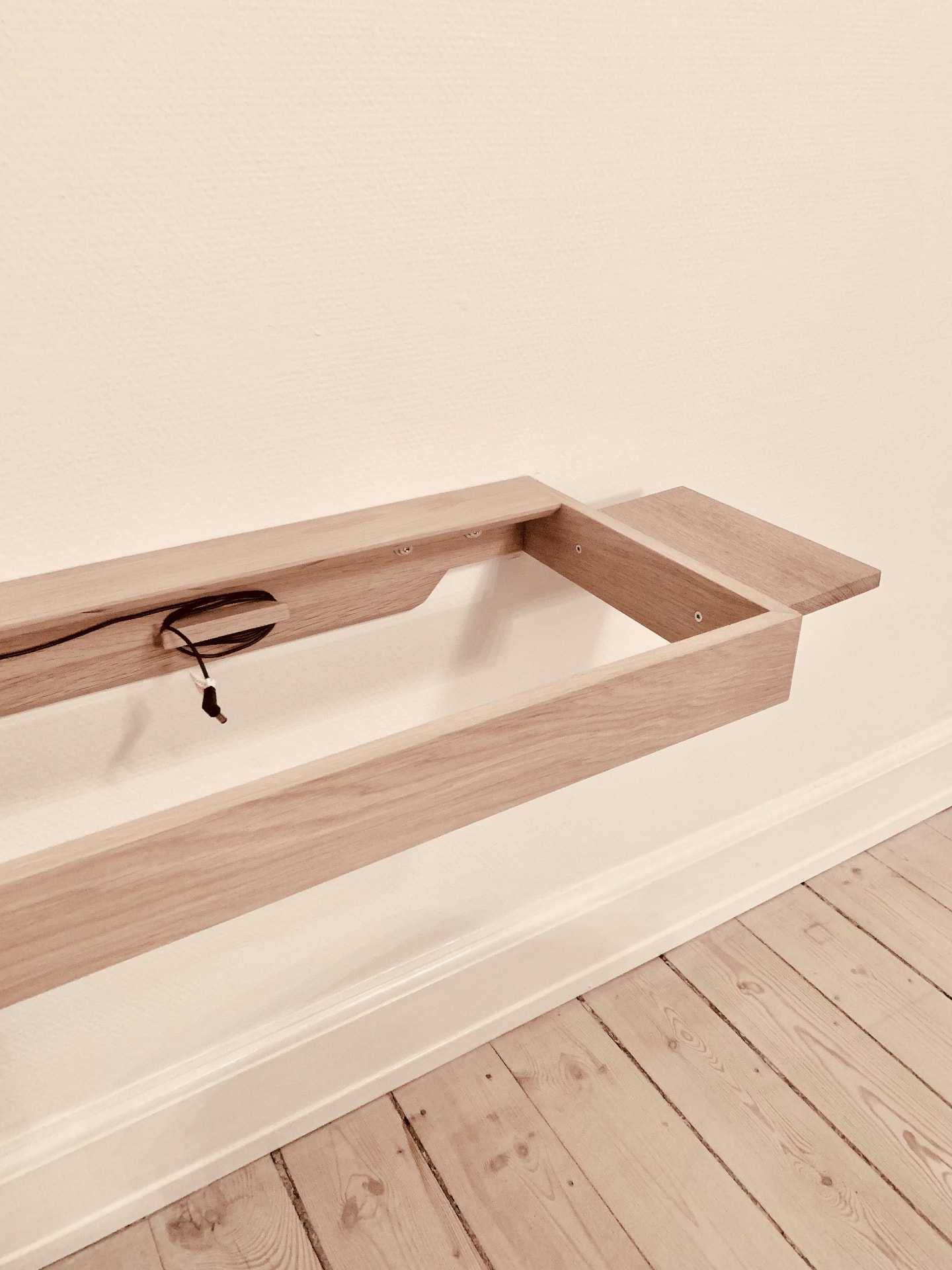 Wall-mounted solid oak piano frame without a piano, showing the open cable channel and side shelf