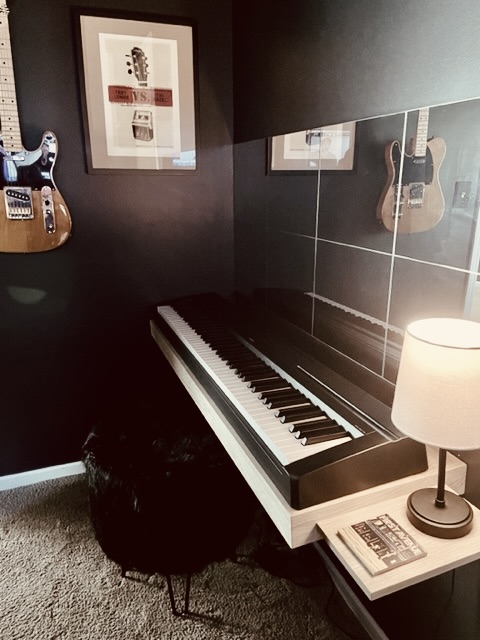 Customer photo of a wall-mounted digital piano stand in a dark music room with guitars on the wall