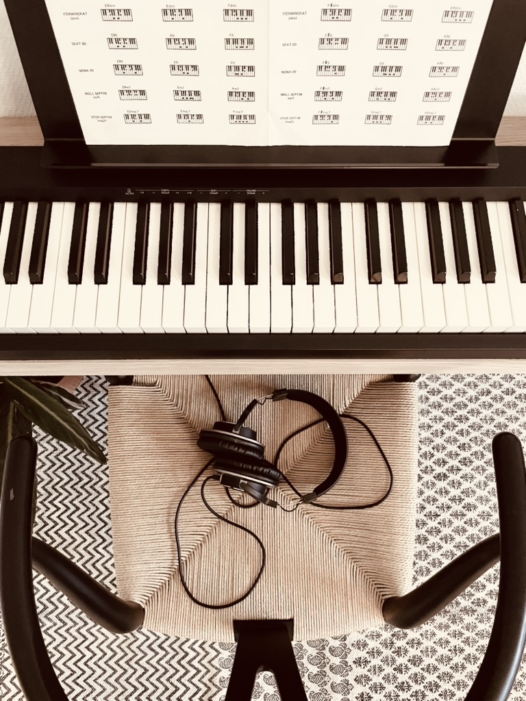 Silent piano practice setup with headphones resting on the chair below a wall-mounted oak piano frame