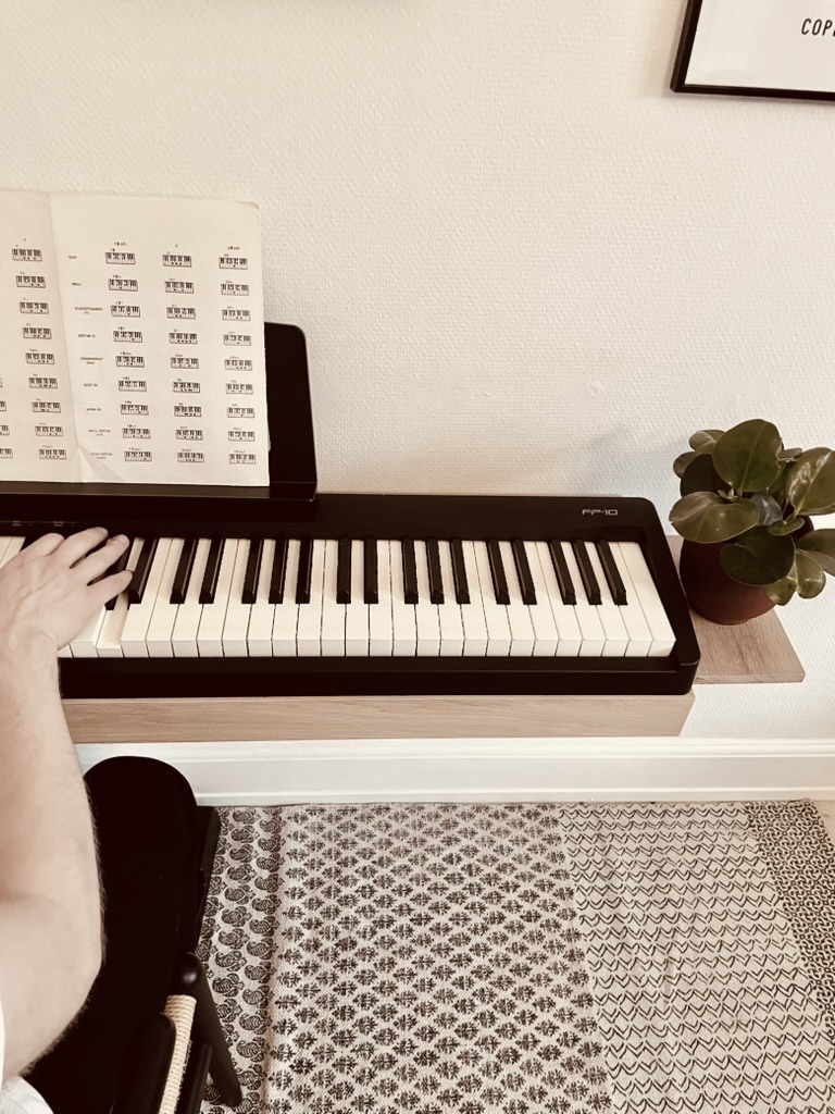 Roland FP-10 on an oak wall-mounted piano shelf with the side shelf holding a potted plant