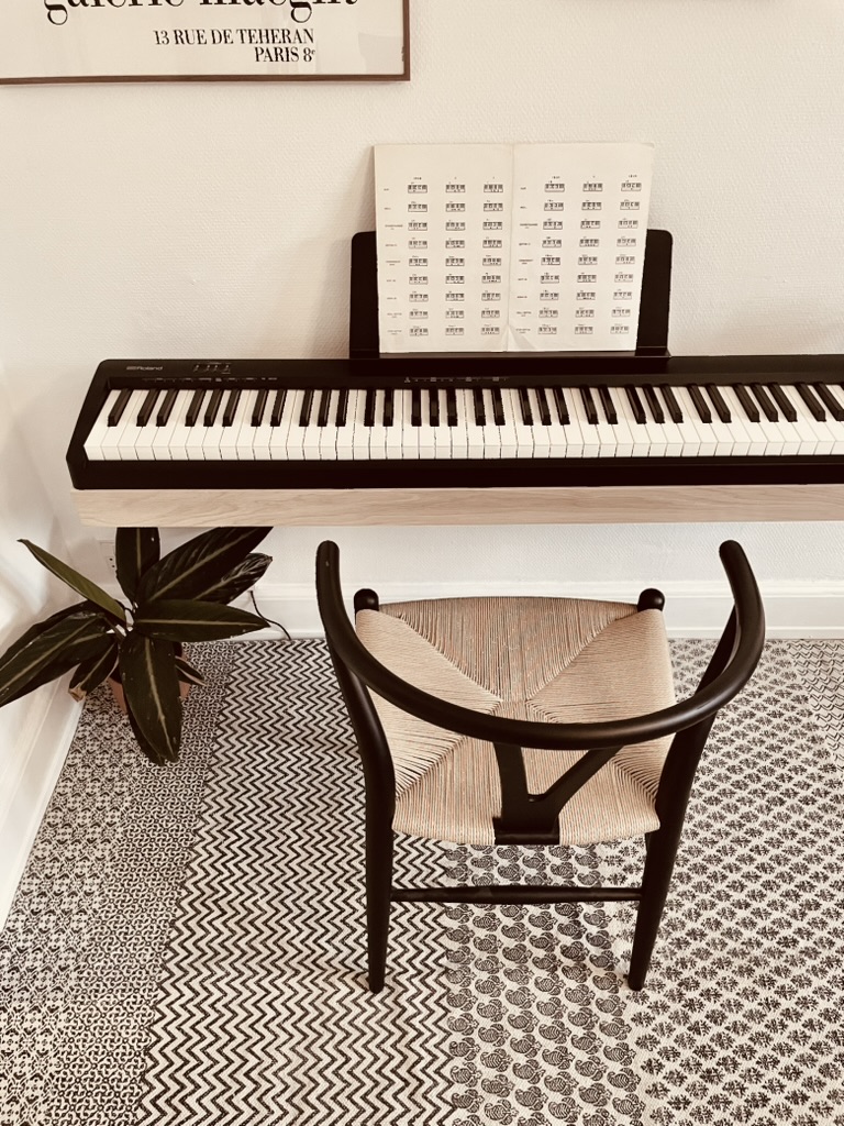 Space-saving floating oak piano frame holding a Roland FP-10 above a wishbone chair