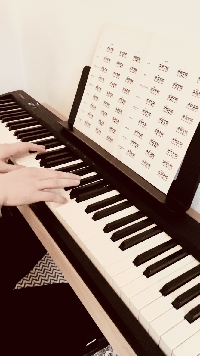 Playing a digital piano on an oak wall-mounted stand with a chord chart on the music rest