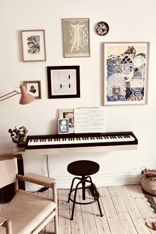 Customer photo of a digital piano on an oak wall shelf beneath a gallery wall of art prints