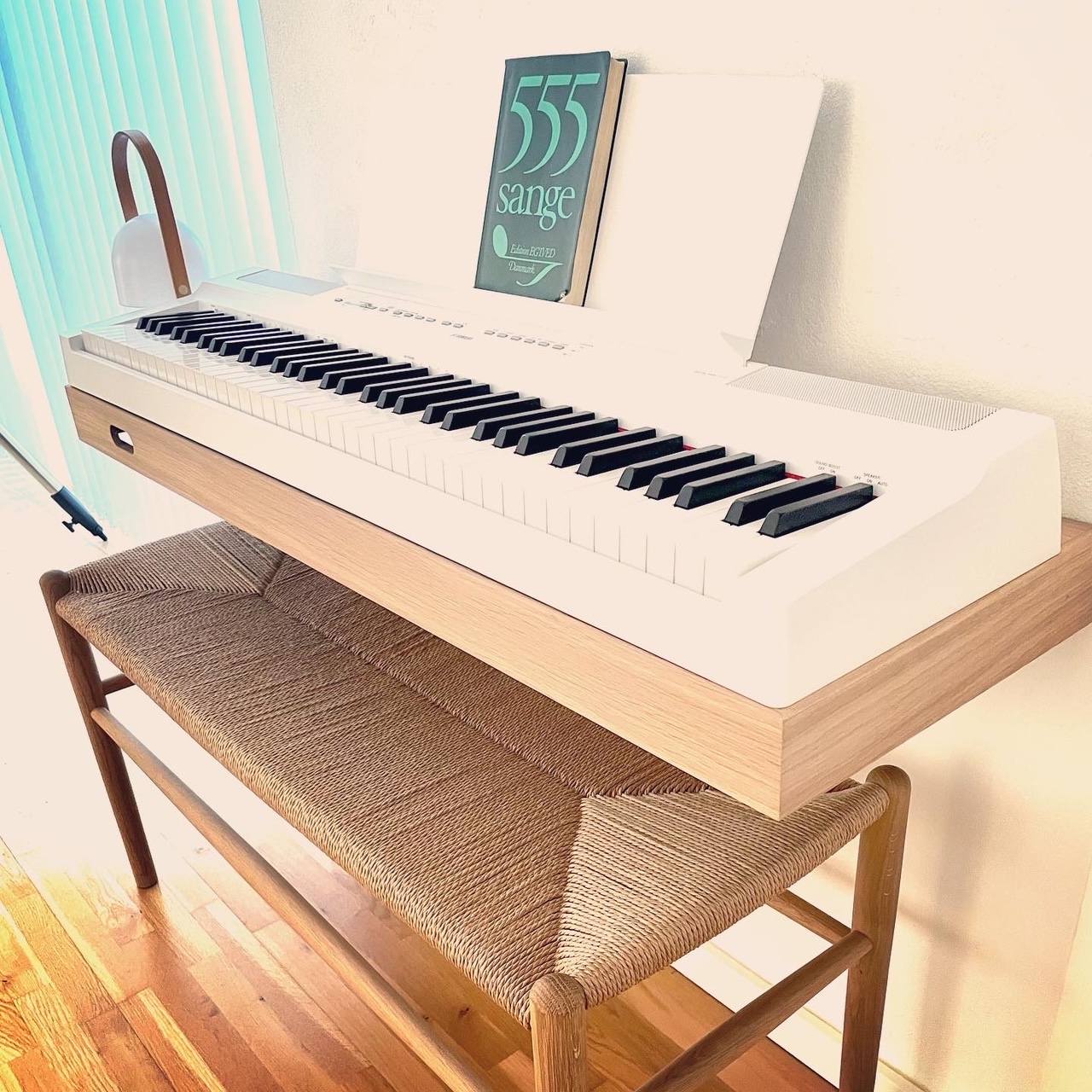 Customer photo of a white Yamaha digital piano on a solid oak floating frame with a songbook and a paper-cord bench