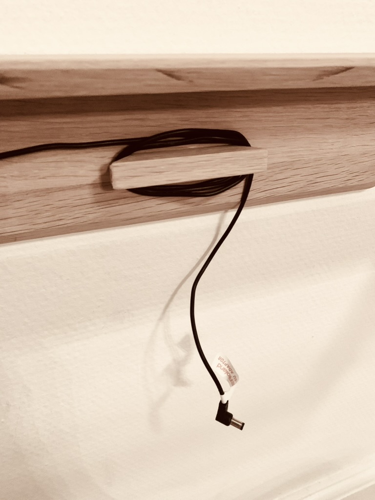 Hidden cable management with an oak power cable holder behind the wall-mounted piano frame