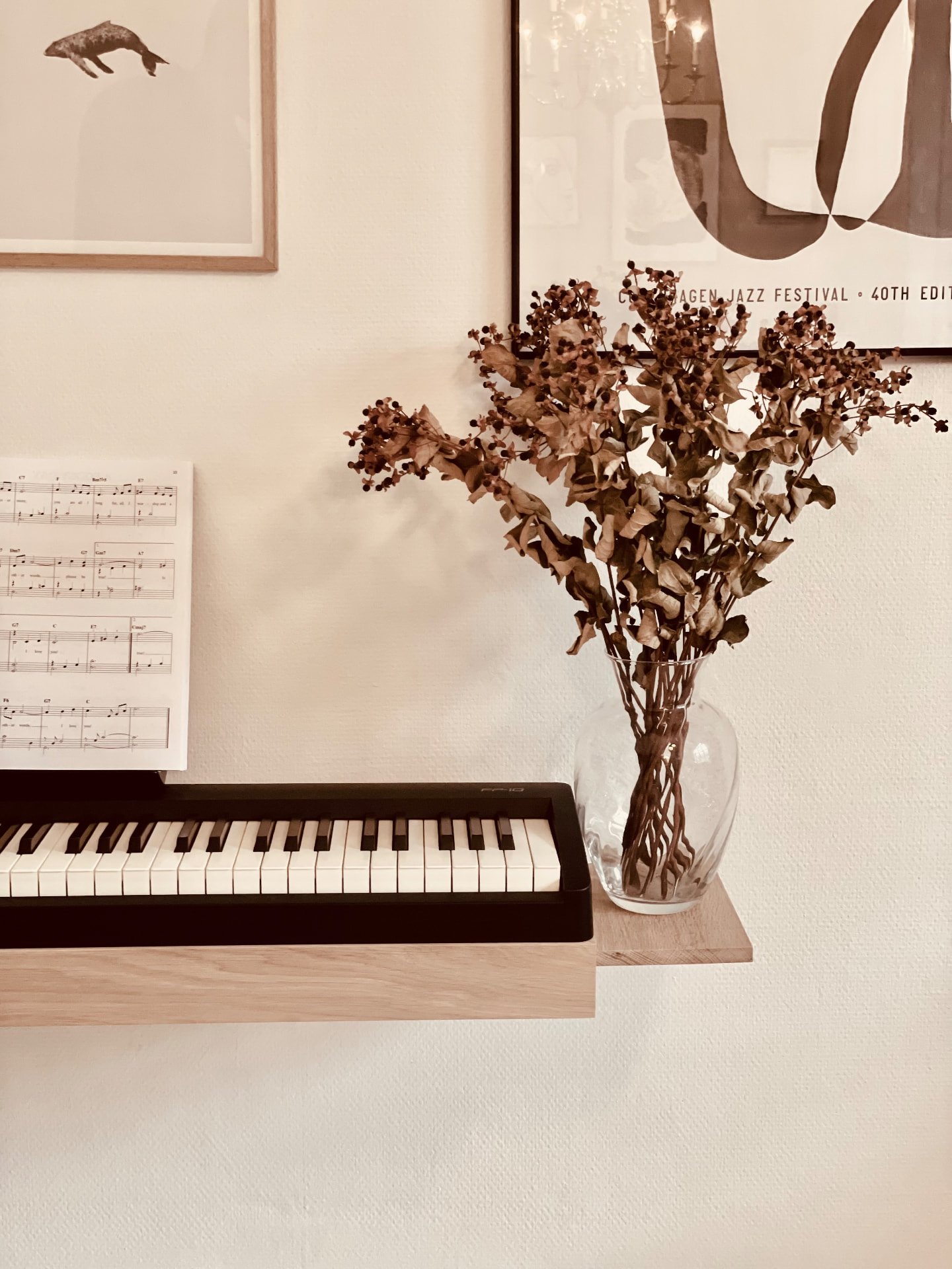 Side shelf detail of an oak wall-mounted digital piano stand with a glass vase