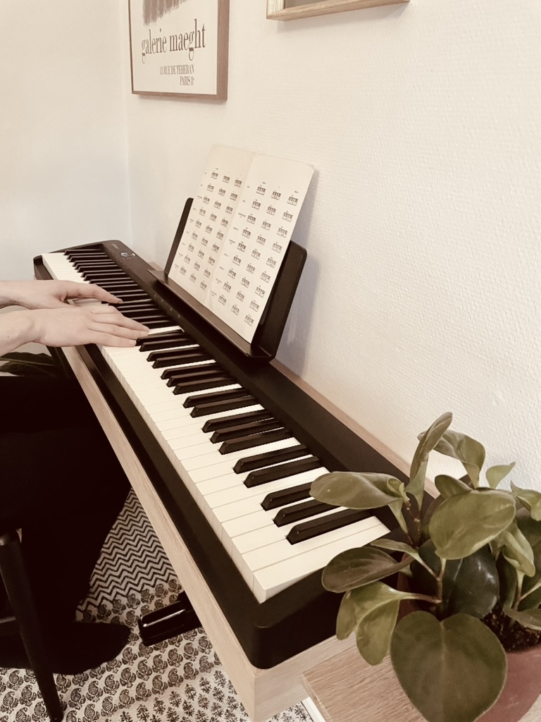 Hands playing a Roland digital piano resting on an oak floating piano frame in a living room